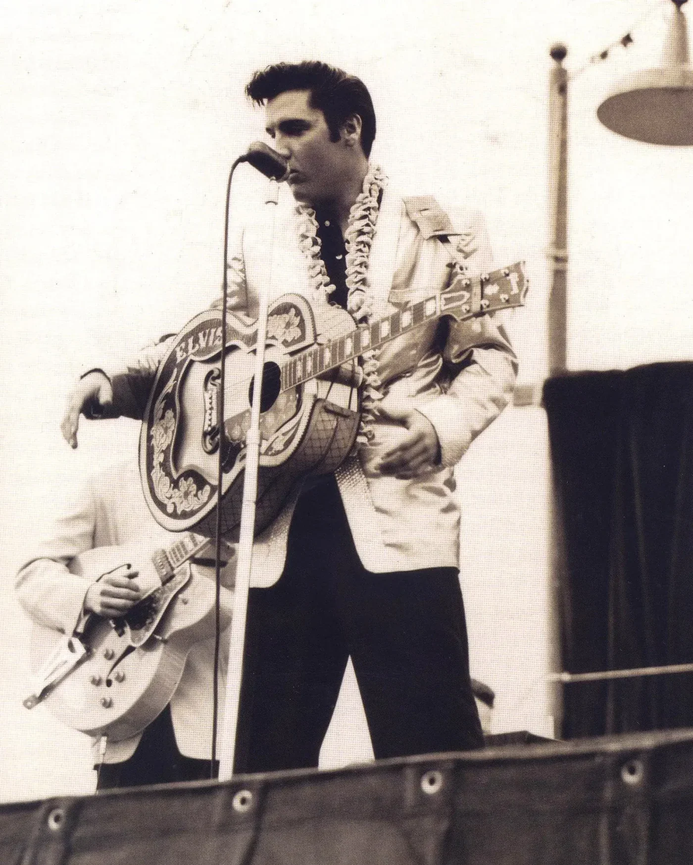 Elvis Presley in a gold jacket and lei, singing and playing guitar during his 1957 Hawaii visit